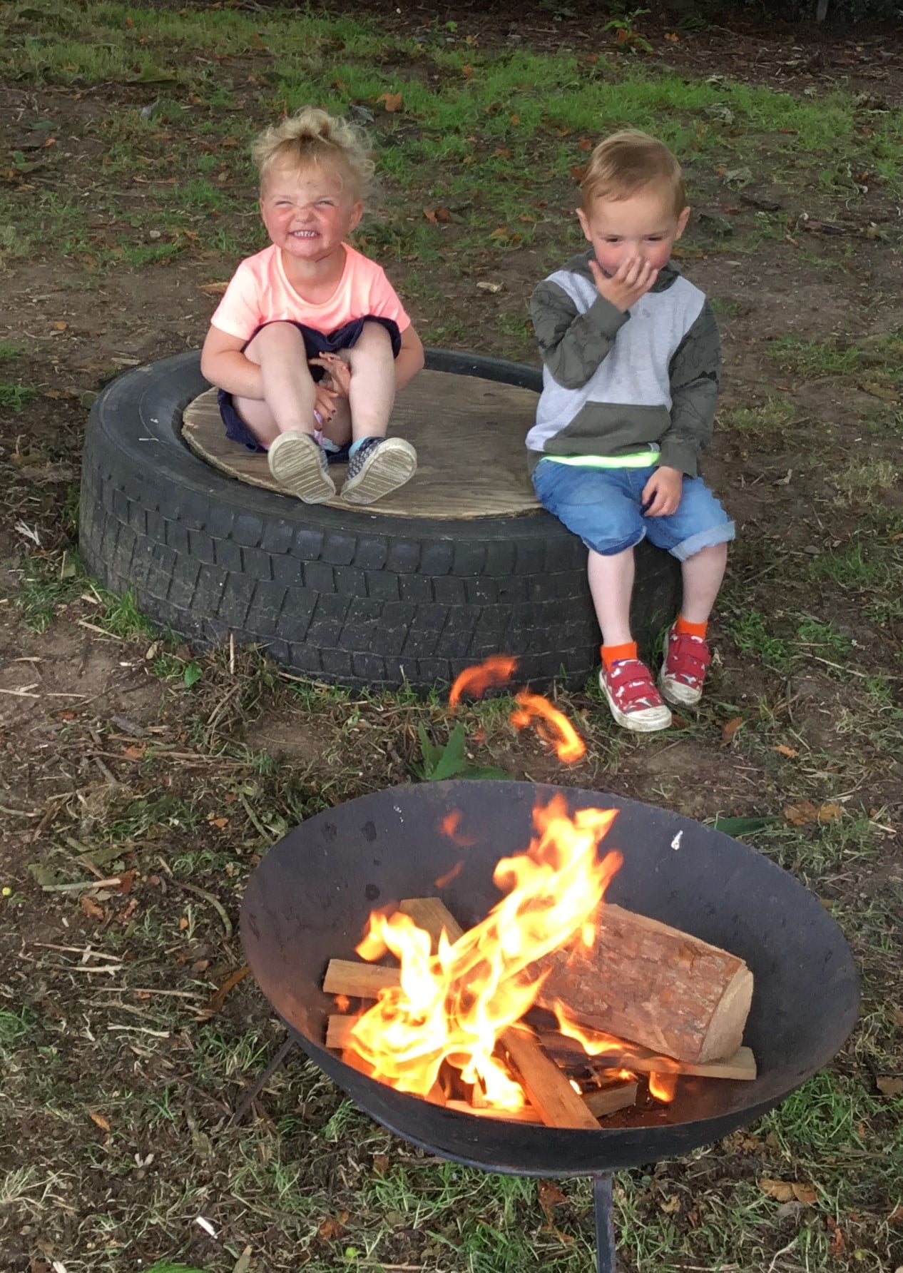 Two children sit a safe distance from a fire pit