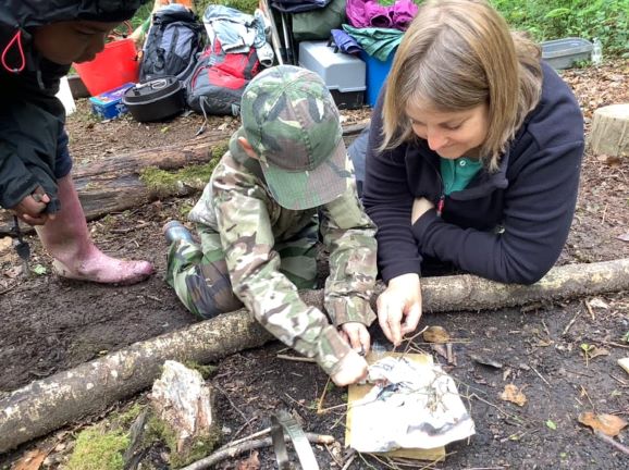 Forest School in action - teacher supervising child starting a campfire